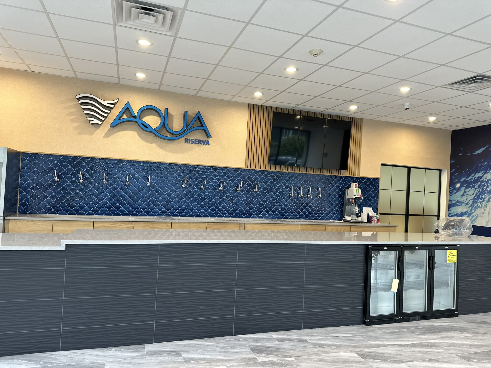 Counter and glass-front coolers at Aqua Riserva in Hawthorne NJ, with the tap wall and signage behind