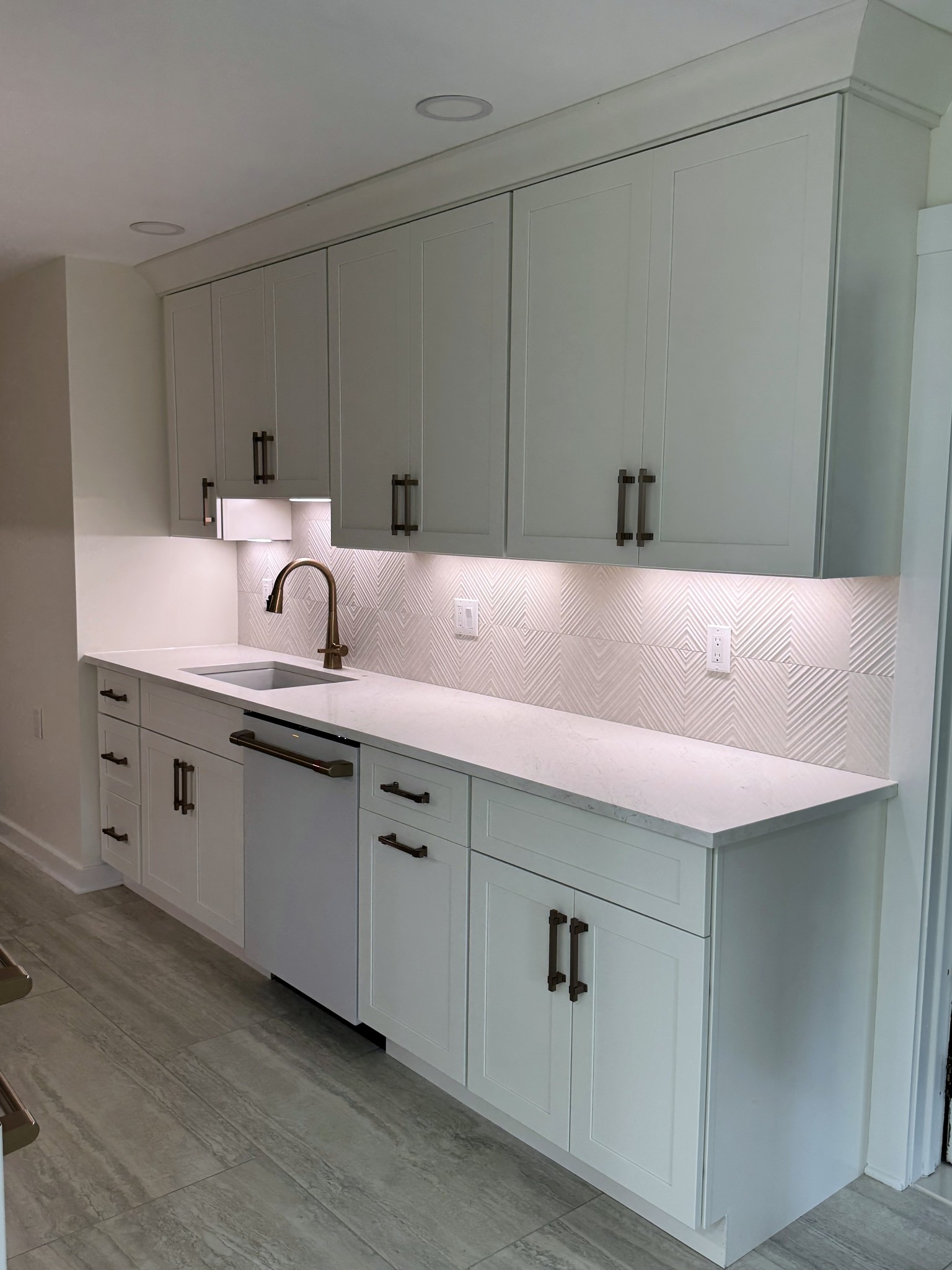 The full cabinet run in the Montclair kitchen, with textured white tile and undercabinet lighting