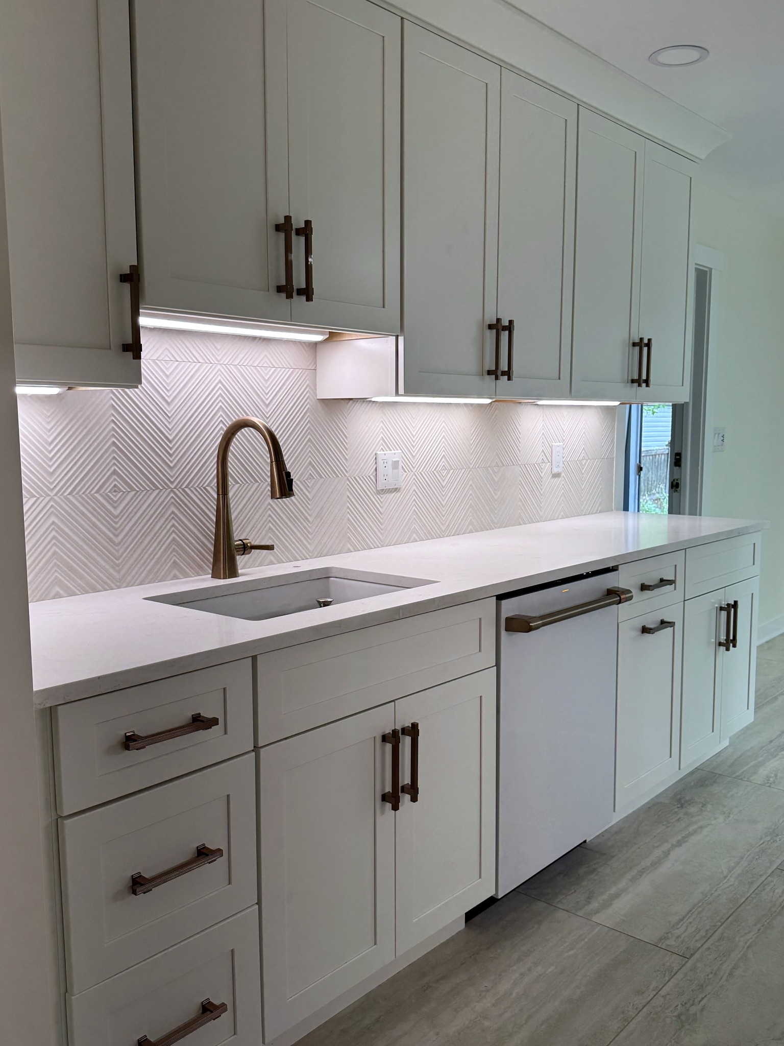 Finished galley kitchen in Montclair, NJ with white shaker cabinets, quartz counter and bronze pulls